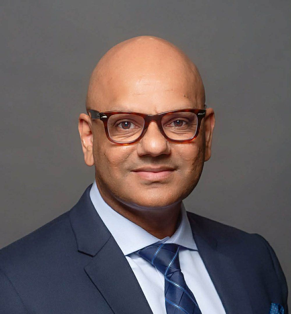 Portrait of Dr. Peter Maharaj in a navy suit and blue tie
