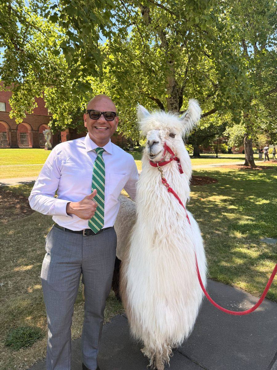 Peter giving a thumbs up beside a llama on a college campus