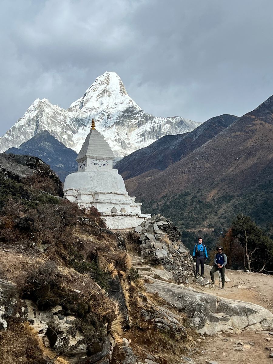 Peter and a fellow trekker beside a white stupa below a snow-capped Himalayan peak