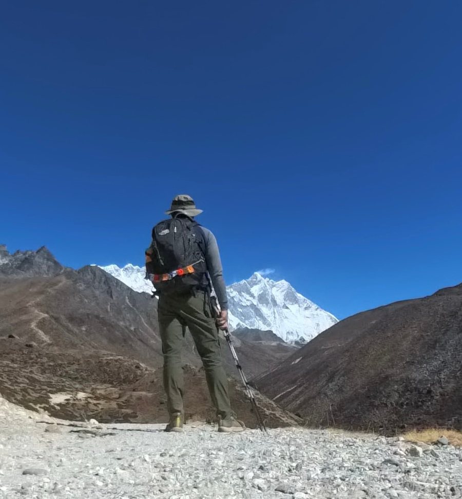 Peter trekking beneath snow-capped Himalayan peaks under a deep blue sky